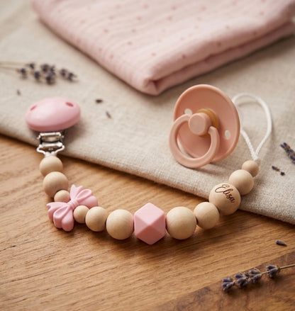 Personalisierte Schnullerkette mit Namen, Gravur, rosa Schleife, Holzperlen und Silikonperlen – individuelles Babygeschenk zur Geburt oder Taufe.